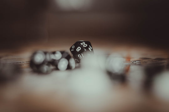 Black polyhedral dice on a blurred tabletop. Image by Nika Benedictova on Unsplash.