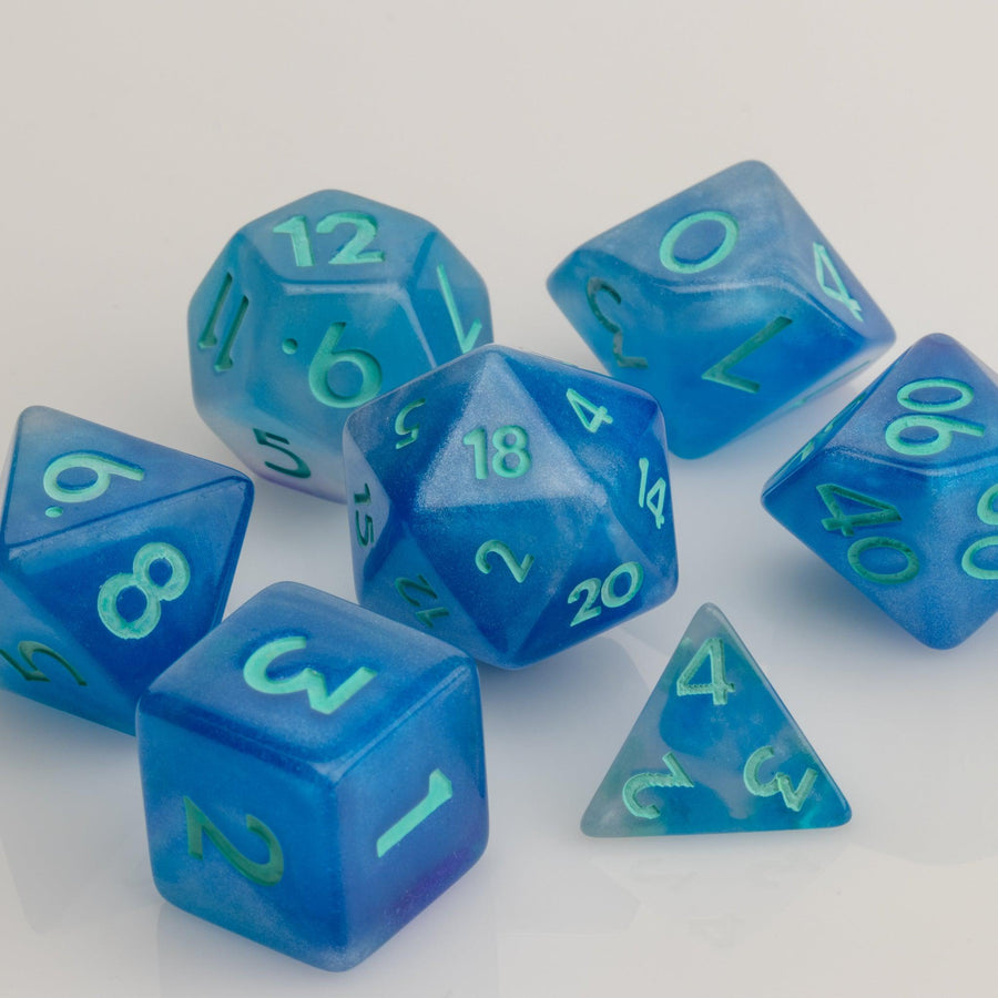 Infinite, cloudy blue dice with glittery inclusions and teal numbering. 7 piece RPG dice set on white background.. 