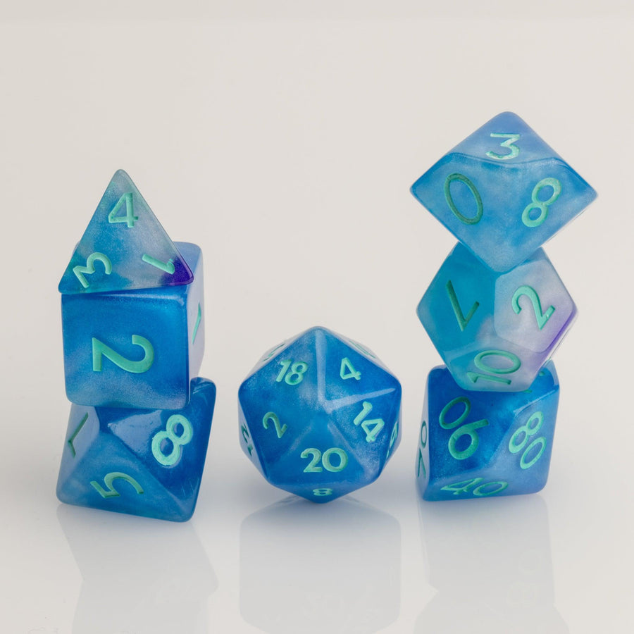 Infinite, cloudy blue dice with glittery inclusions and teal numbering. 7 piece RPG dice set stacked on white background.. 
