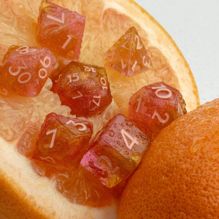 Pamplemousse, 7 piece RPG dice set lain on grapefruit.