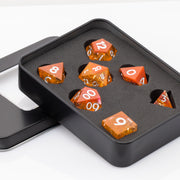 Sunfire, swirling orange and red handmade DND dice set in decorative tin on a white background.